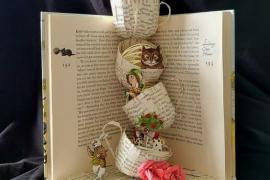 A photograph of a book, standing vertically and open in the middle. Several stacked teacups made of pages from the book are in the center of the open pages. 