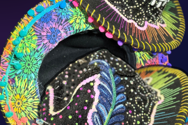 Black felt hat decorated with rhinestones, hanging charms, sequin appliques, rainbow embroidery thread, and pompom trim.