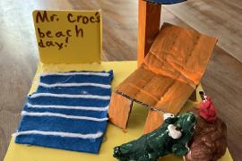 It is a small replica of a beach with a umbrella, beach towel, beach chair, and stand with a Hawaiian drink that Mr. Croc is trying to get.