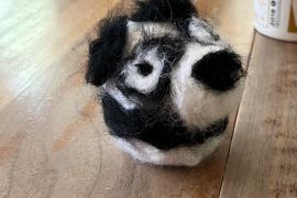 It is a needle-felted representation of a black-and-white panda. 