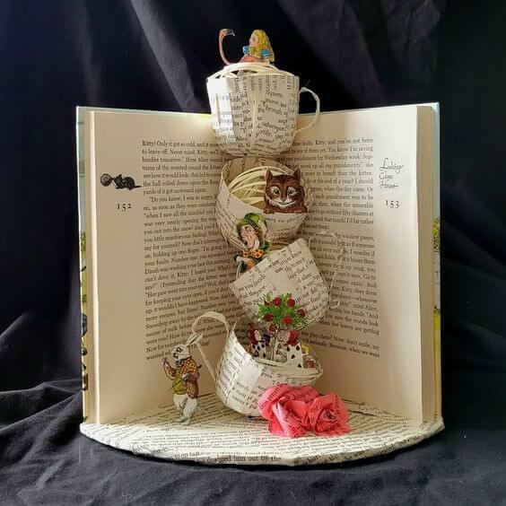 A photograph of a book, standing vertically and open in the middle. Several stacked teacups made of pages from the book are in the center of the open pages. 