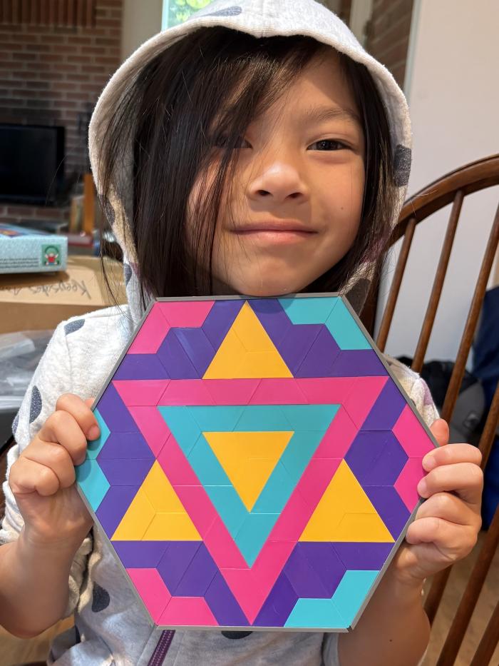 Eva is holding up a colorful star mosaic pattern that she created. 