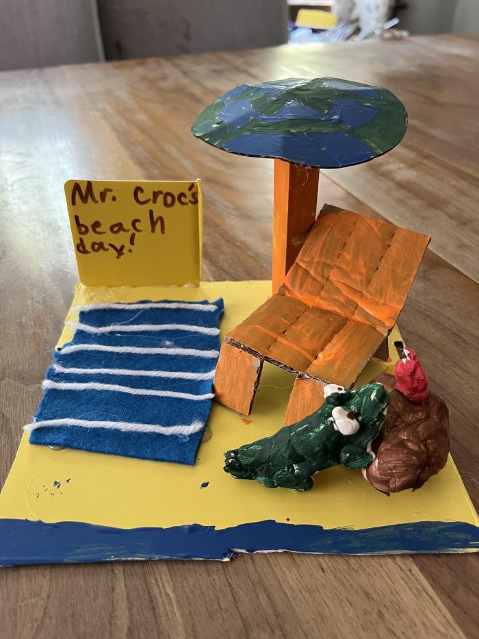 It is a small replica of a beach with a umbrella, beach towel, beach chair, and stand with a Hawaiian drink that Mr. Croc is trying to get.