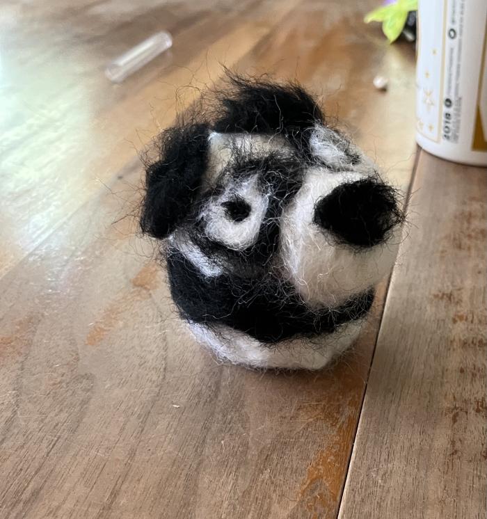 It is a needle-felted representation of a black-and-white panda. 