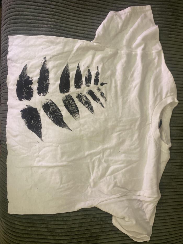 Photo of a white T-Shirt with an imprint of black leaves covering the left side of the shirt.